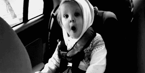 a toddler waves her arms and bounces excitedly in her car seat