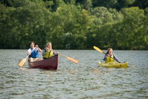Two women paddle a canoe close to another woman in a kayak on Lake Winona