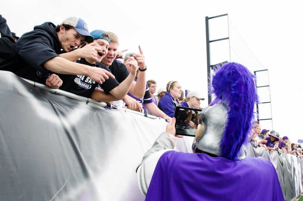 Cheering fans in the student section at a football game with Wazoo taking a picture of them.