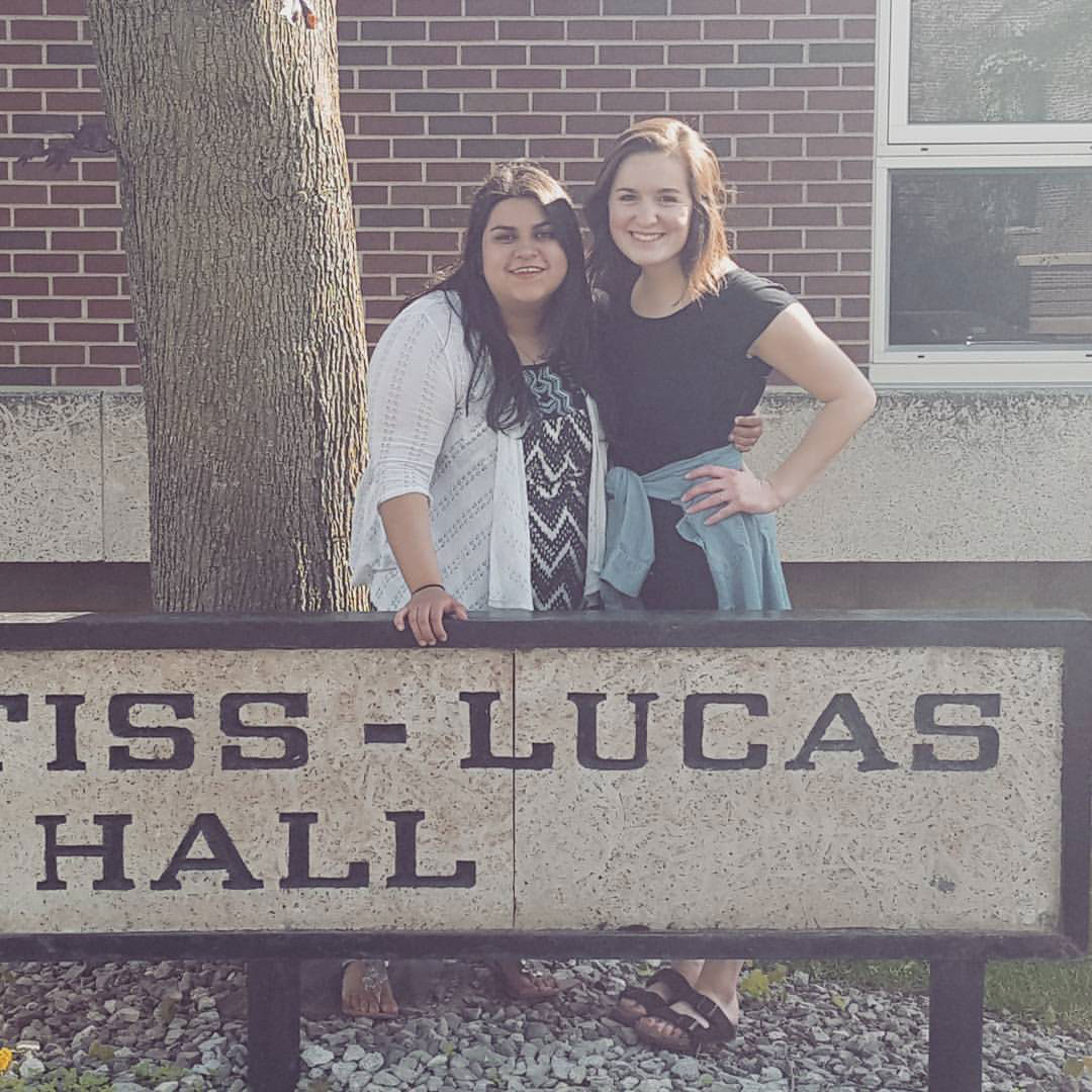 Lizette and Erin, Freshman year roommates, standing by the Prentiss-Lucas Hall sign