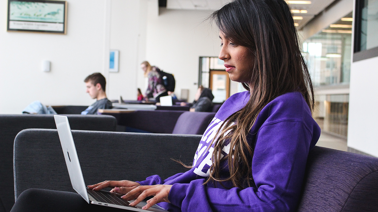 A female student works on her laptop inthe College of Business Engagement Center