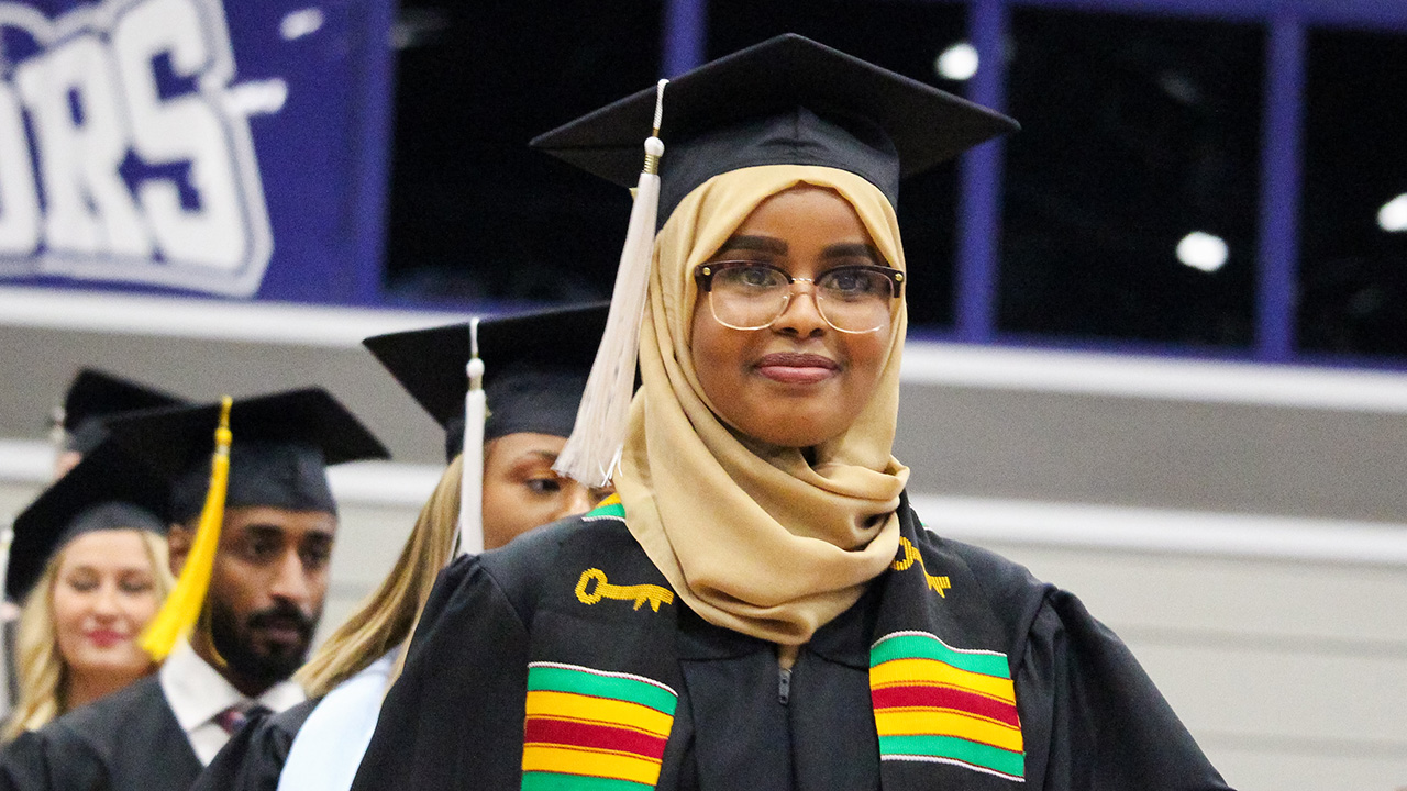 A female graduate dressed in commencement cap and gown, hijab and KEAP Center stole.