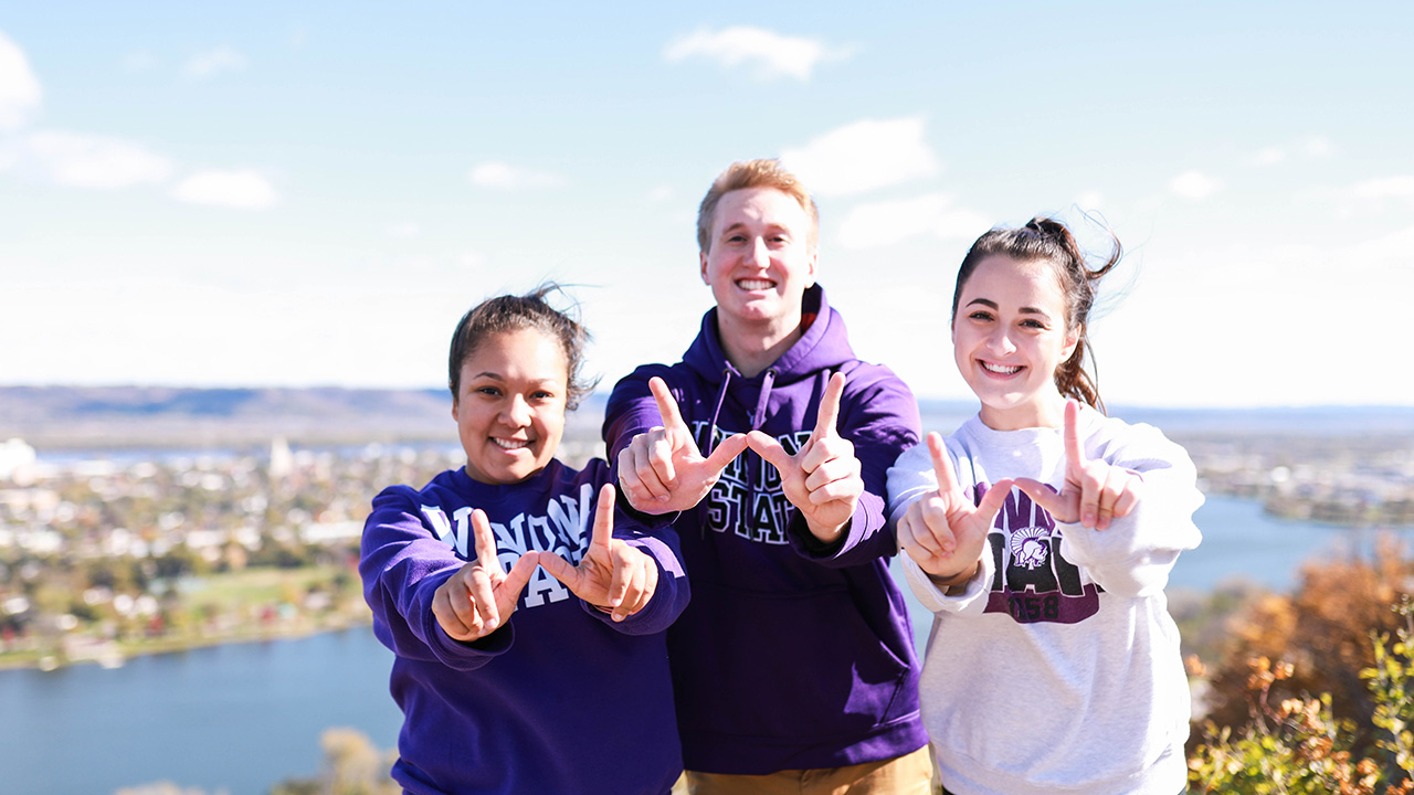 Three WSU students pose together and make a W shape with their hands.