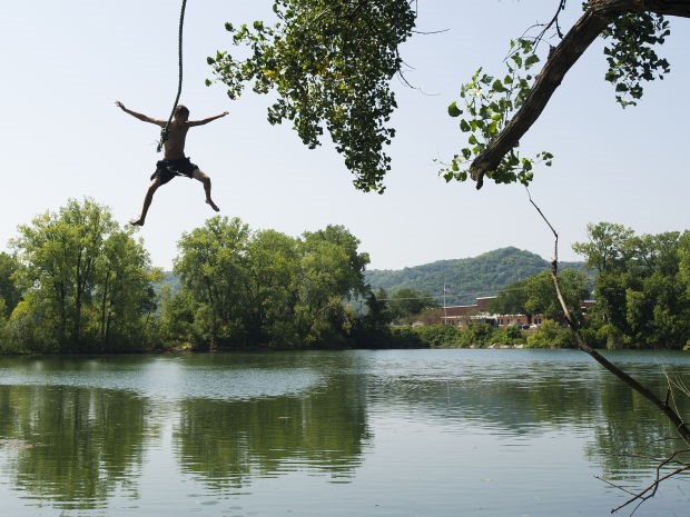 a person jumping into a lake from a rope swing