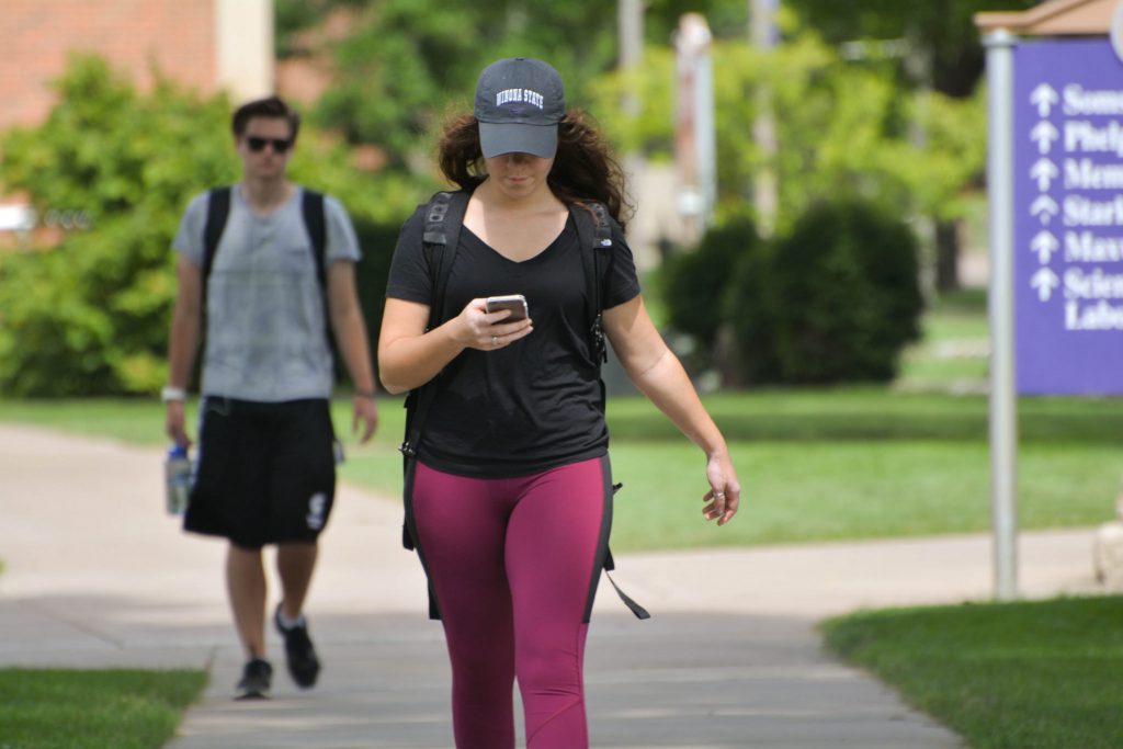 Student texting while walking across campus.