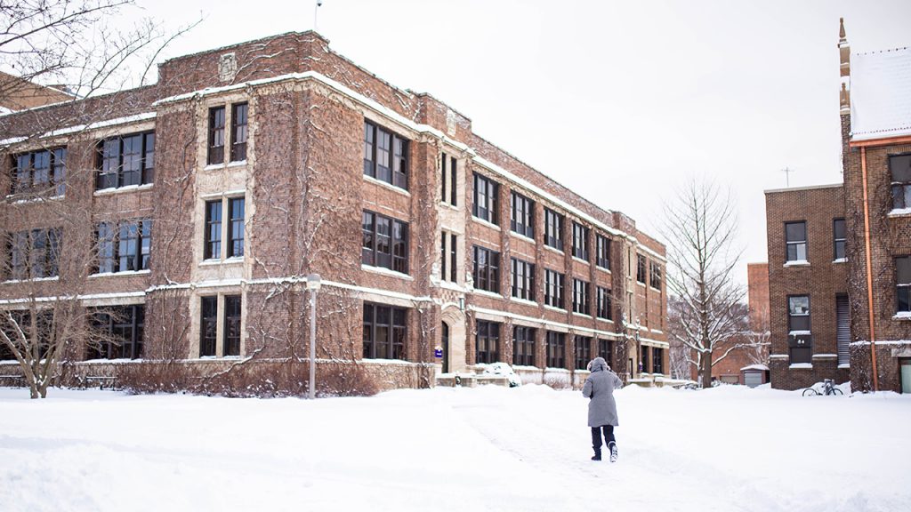 qA student bundled up in a coat walks toward Somsen and Phelps Halls while campus is covered in snow